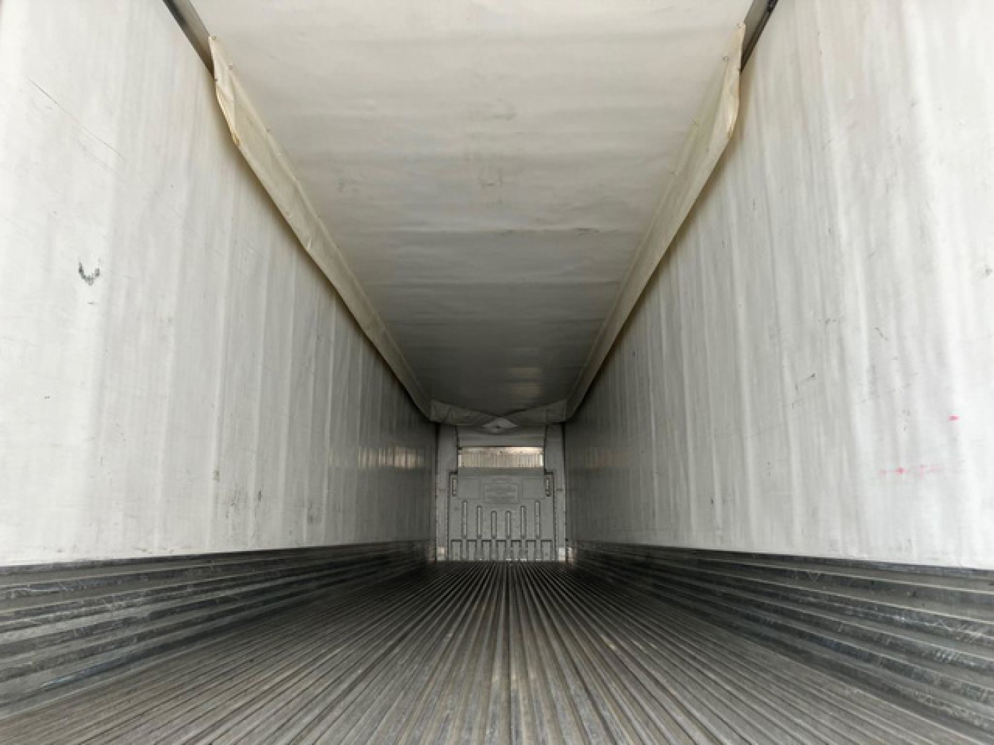 Trailer interior showing longitudinal walls and ribbed metal floor with a doorway at far end.