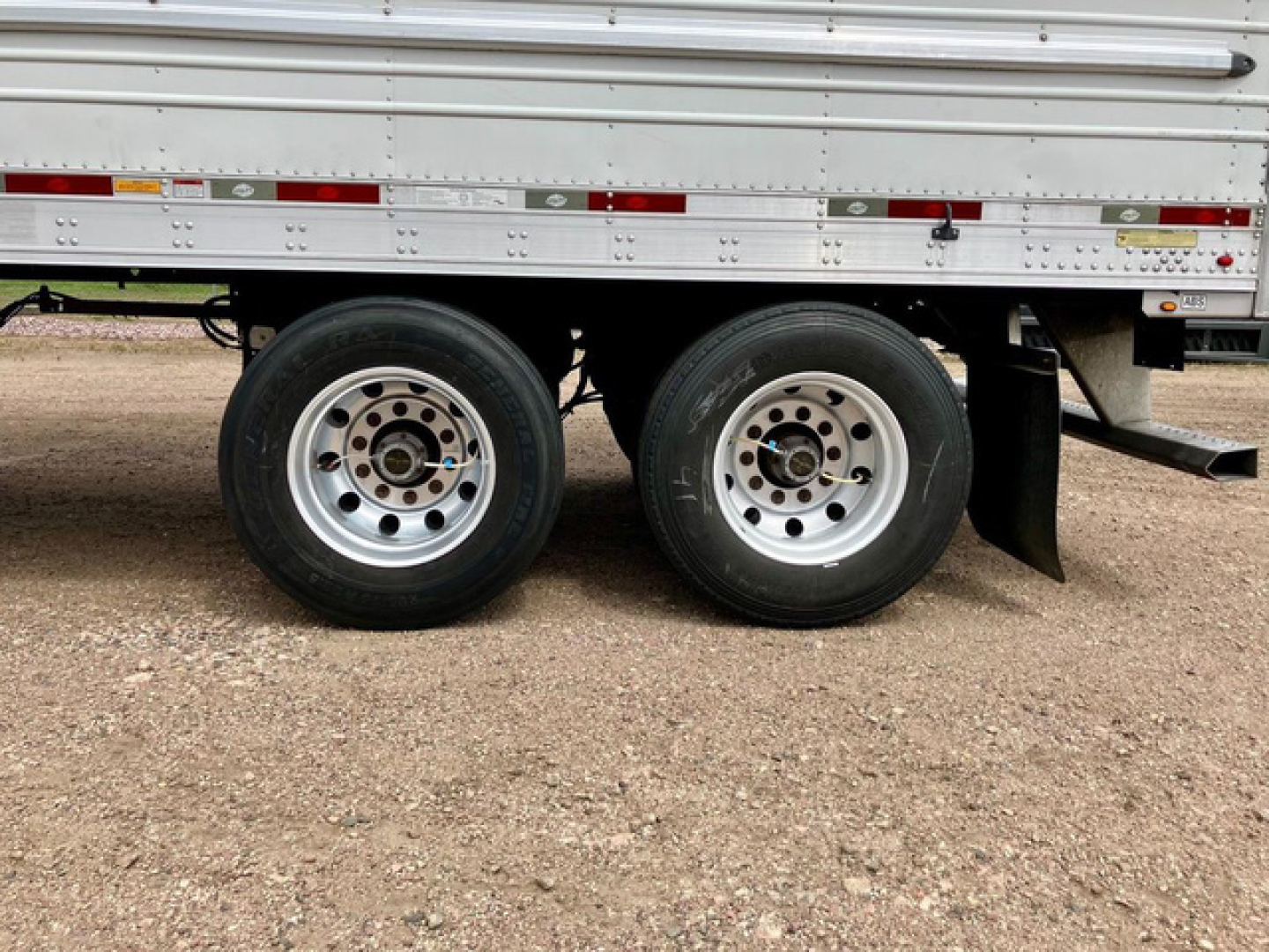 Dual-axle trailer tire assembly on a refrigerated trailer with metal side walls and bumper undercarriage.