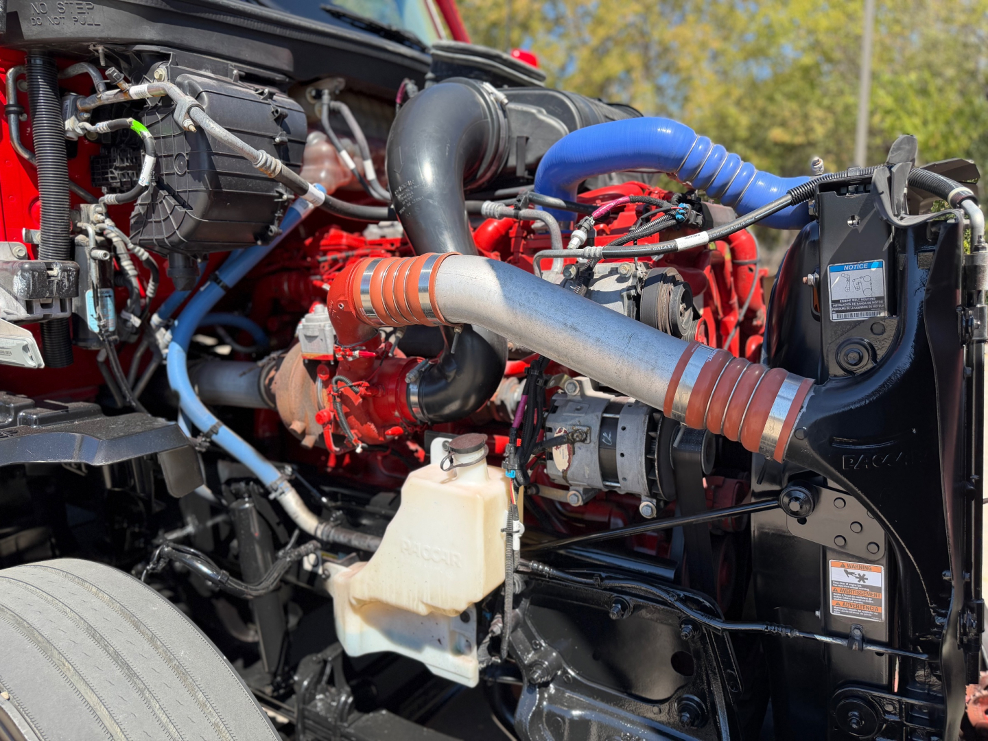 Kenworth T680 engine bay showing coolant reservoir, turbo hose, blue silicone hose, and diesel engine components in red and black colors.