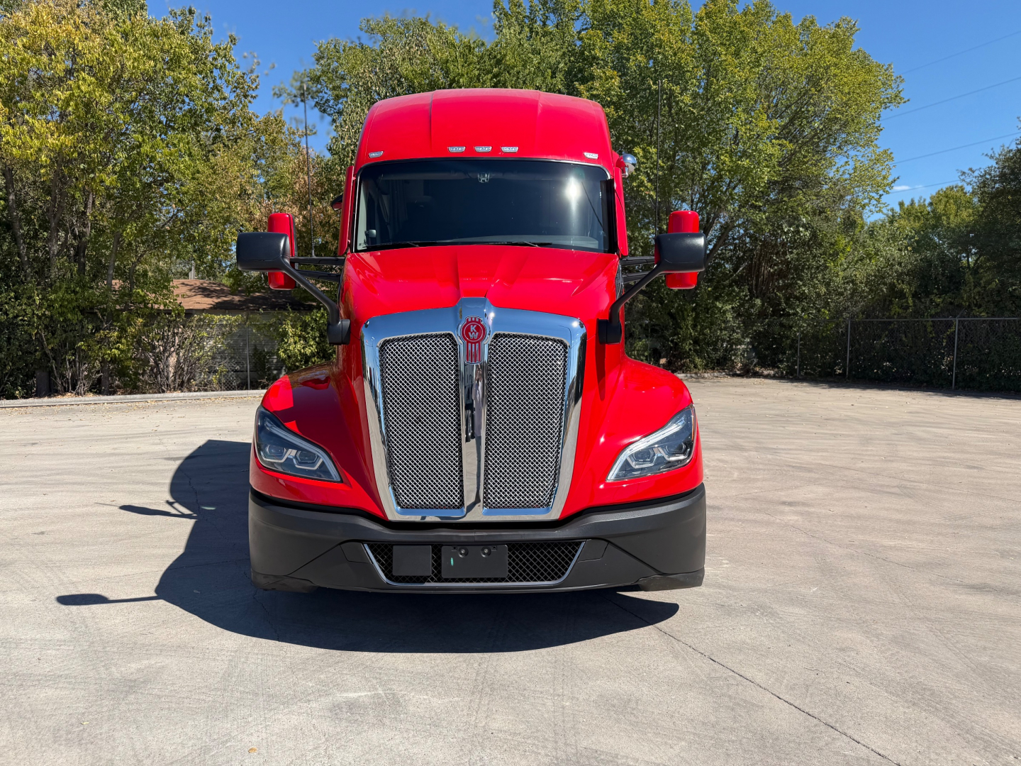 Kenworth T680 head-on view showing bold chrome grille, red cab, black bumper, large side mirrors, and clear windshield.