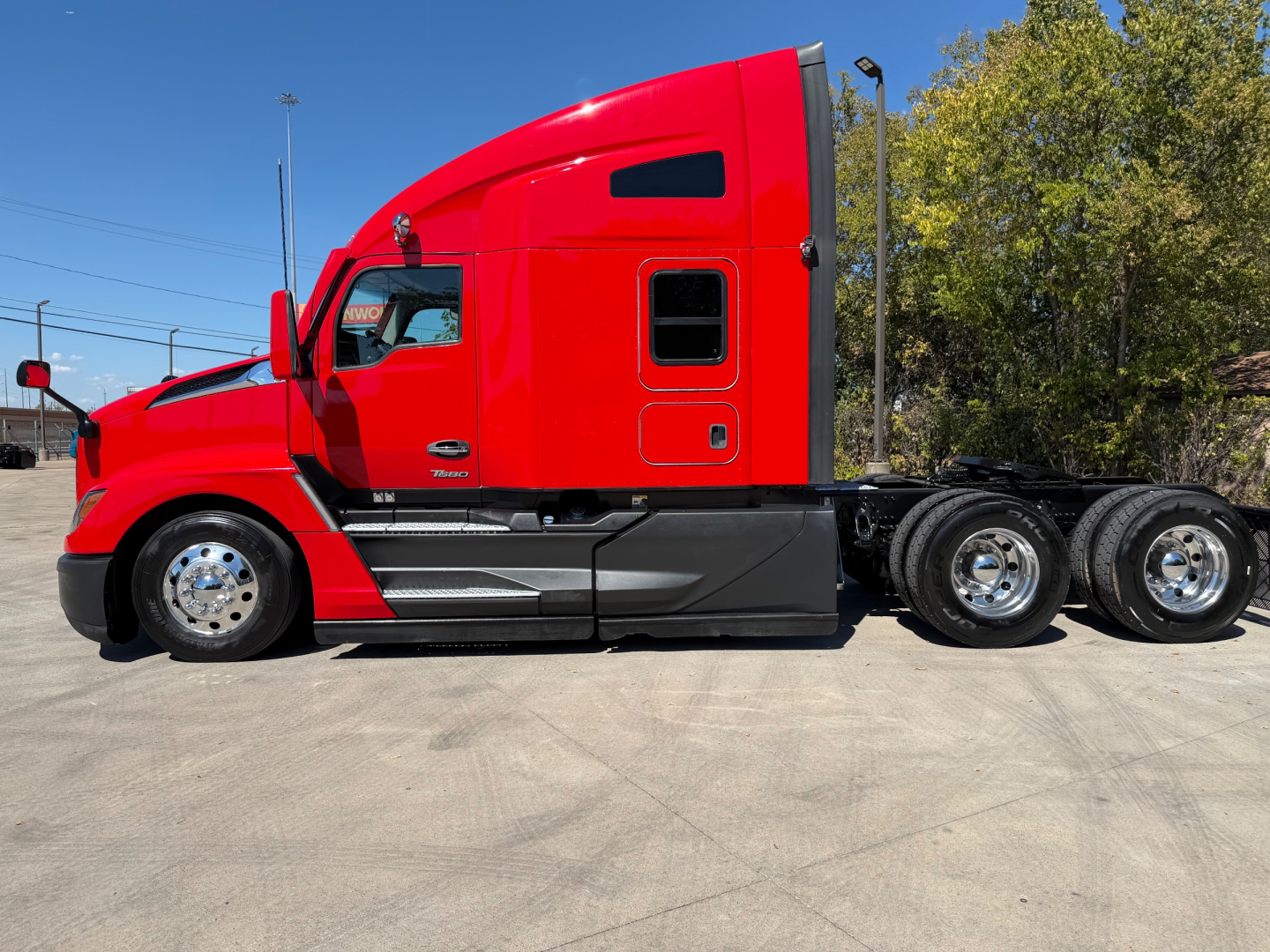 Kenworth T680 tractor in red profile view showing cab, sleeper, and dual rear axles with chrome wheels.