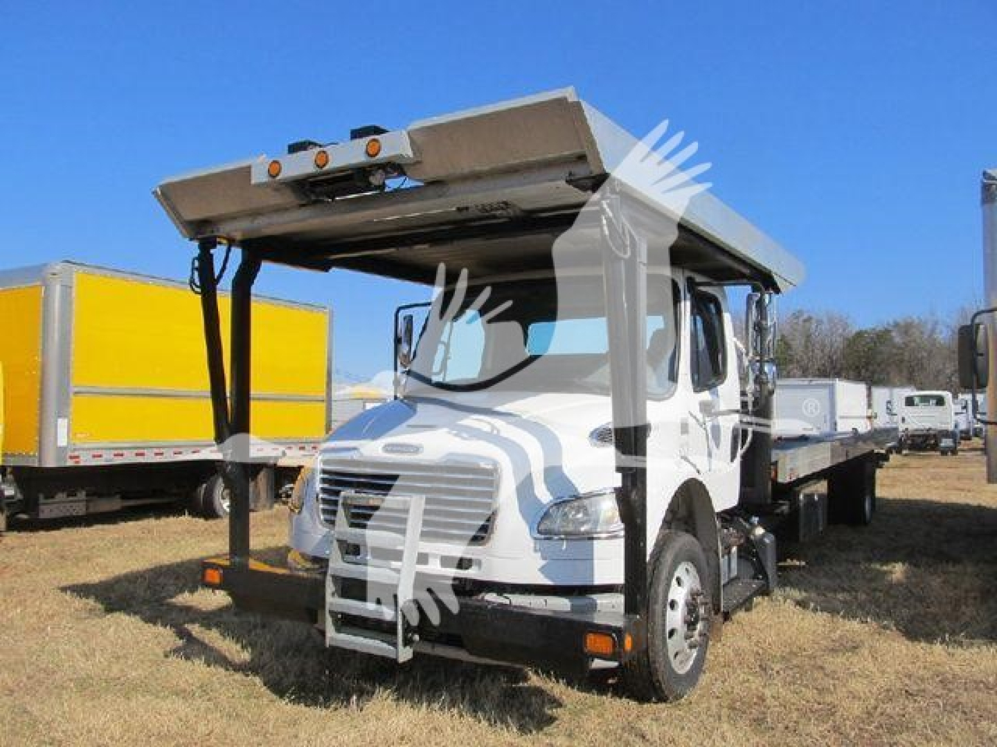 Truck front cab of a 2019 Freightliner M2 106 auto carrier with raised loading ramp and trailer in background