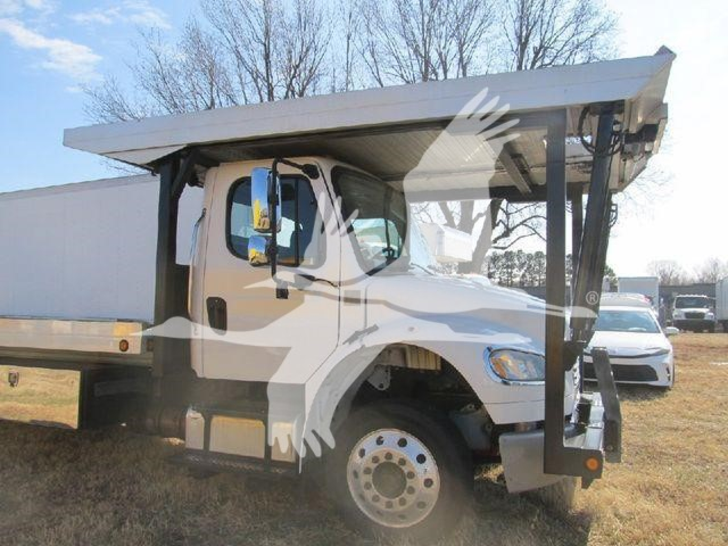 Truck cab and dump bed on Freightliner M2 106 rear view showing auto carrier configuration and front wheel, side mirror, and hydraulic dump mechanism.