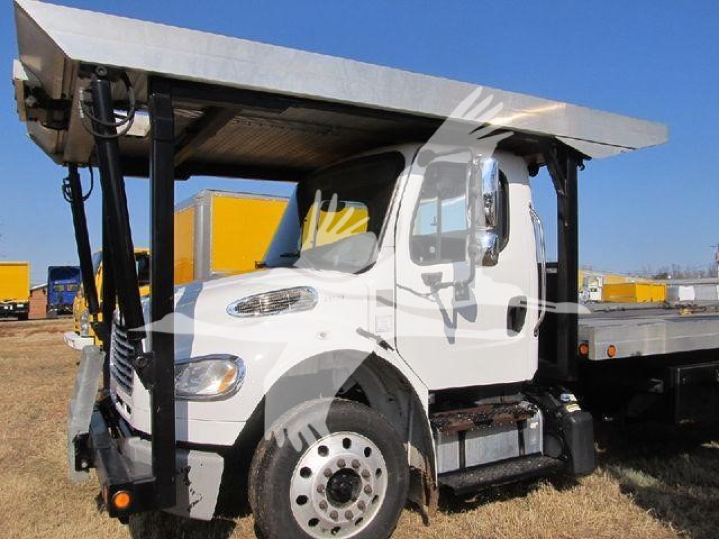Freightliner M2 106 auto carrier truck with tilted flatbed in-service showing side view and front wheel detail.