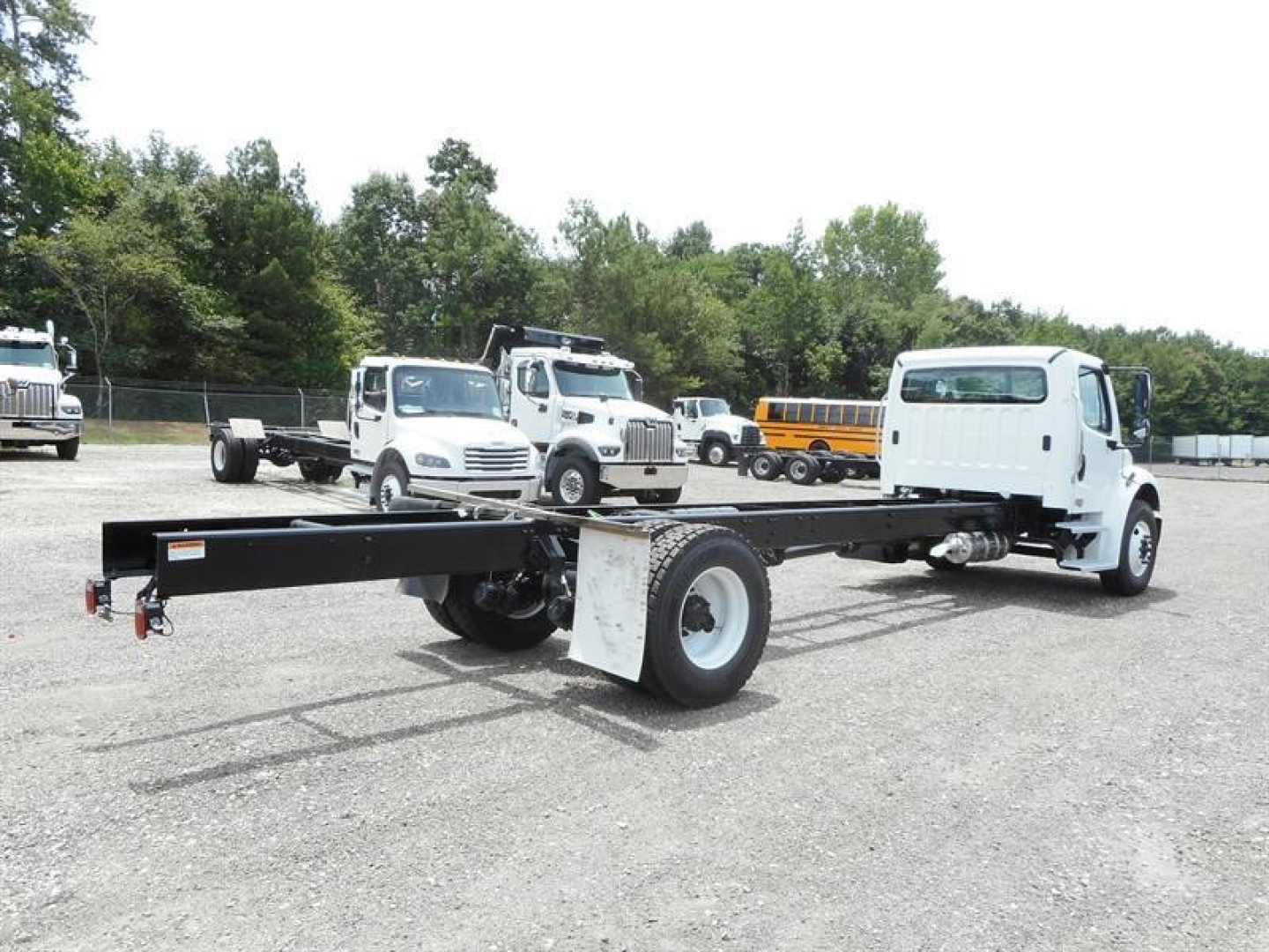 Freightliner M2 106 cab and chassis showing a long black frame and white cab in a gravel lot with other trucks in background.