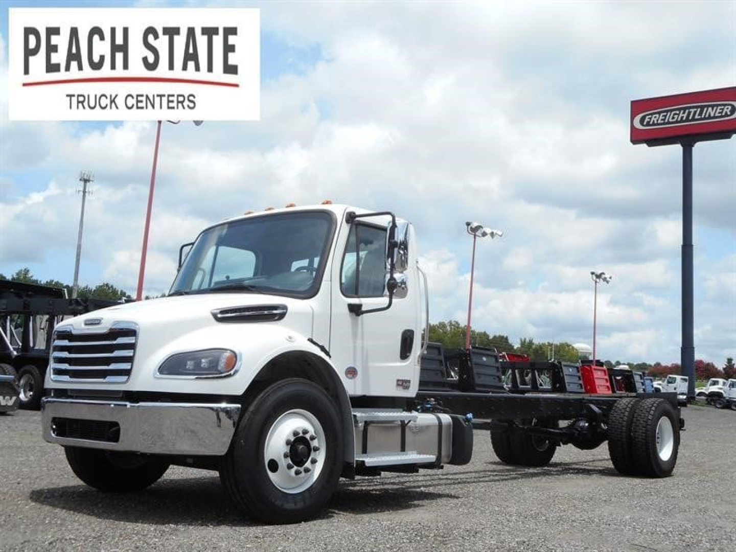 Freightliner M2 106 cab and chassis truck in a dealership lot with Peach State Truck Centers sign and Freightliner sign in background.