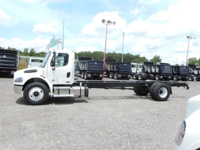 Freightliner M2 106 cab chassis side view showing truck chassis and front cab, with other trucks in lot in background.