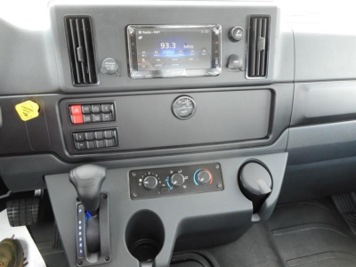 Cab interior of a 2027 Freightliner M2 106 showing center console with radio display reading 93.3 MHz, climate control dials, gear shifter on left, cup holder, and dashboard buttons.
