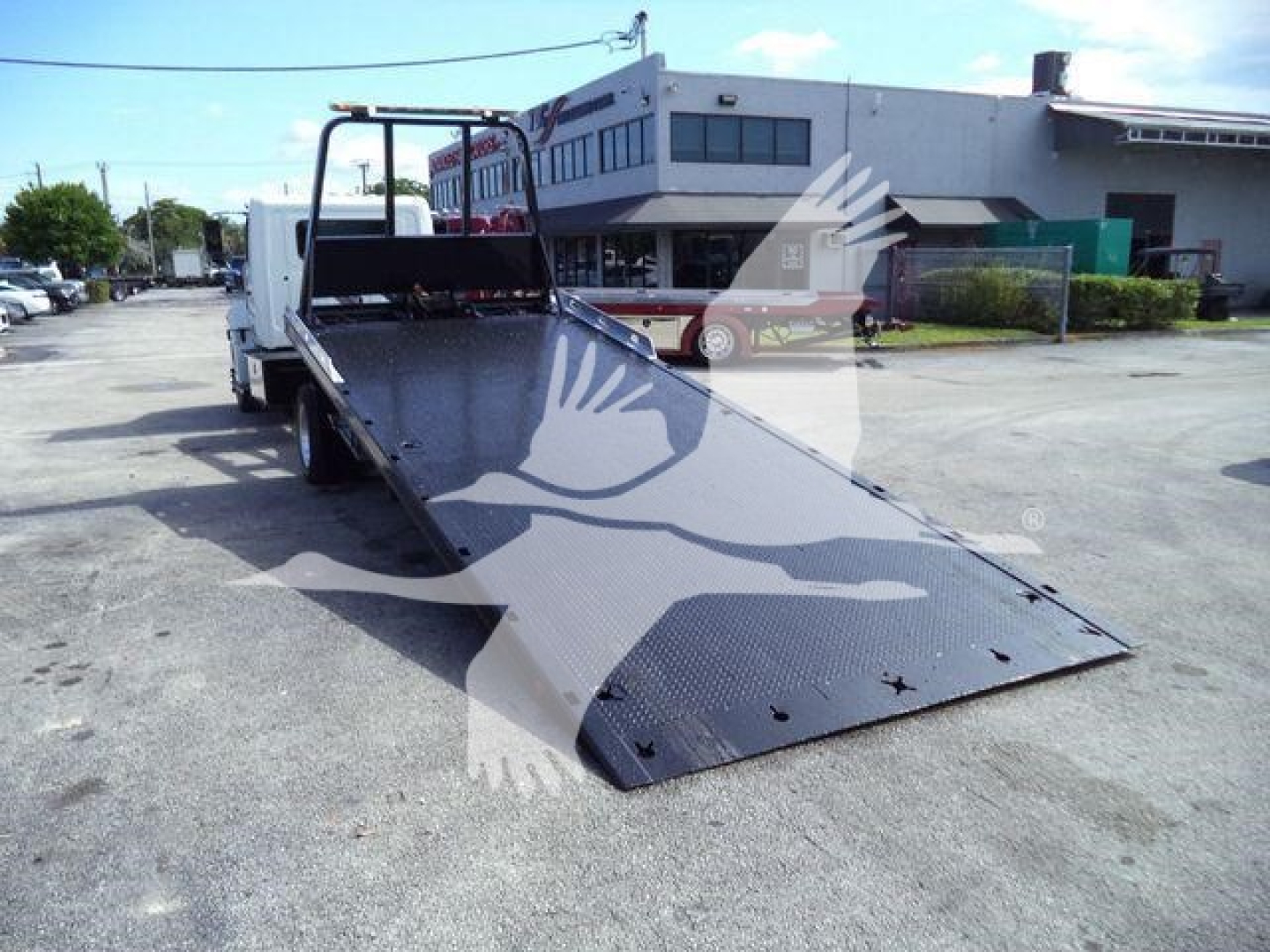 Hino 258A rollback truck with lowered ramp and flatbed in exterior lot showing winch controls and rear ramps.