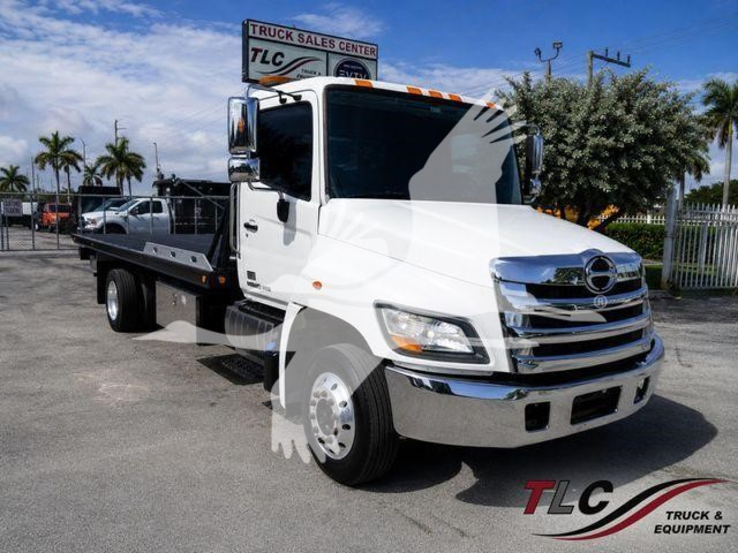 Hino 258Al rollback tow truck front view with flatbed and chrome grille, light bar, and TLC Truck Sales Center logo watermark.