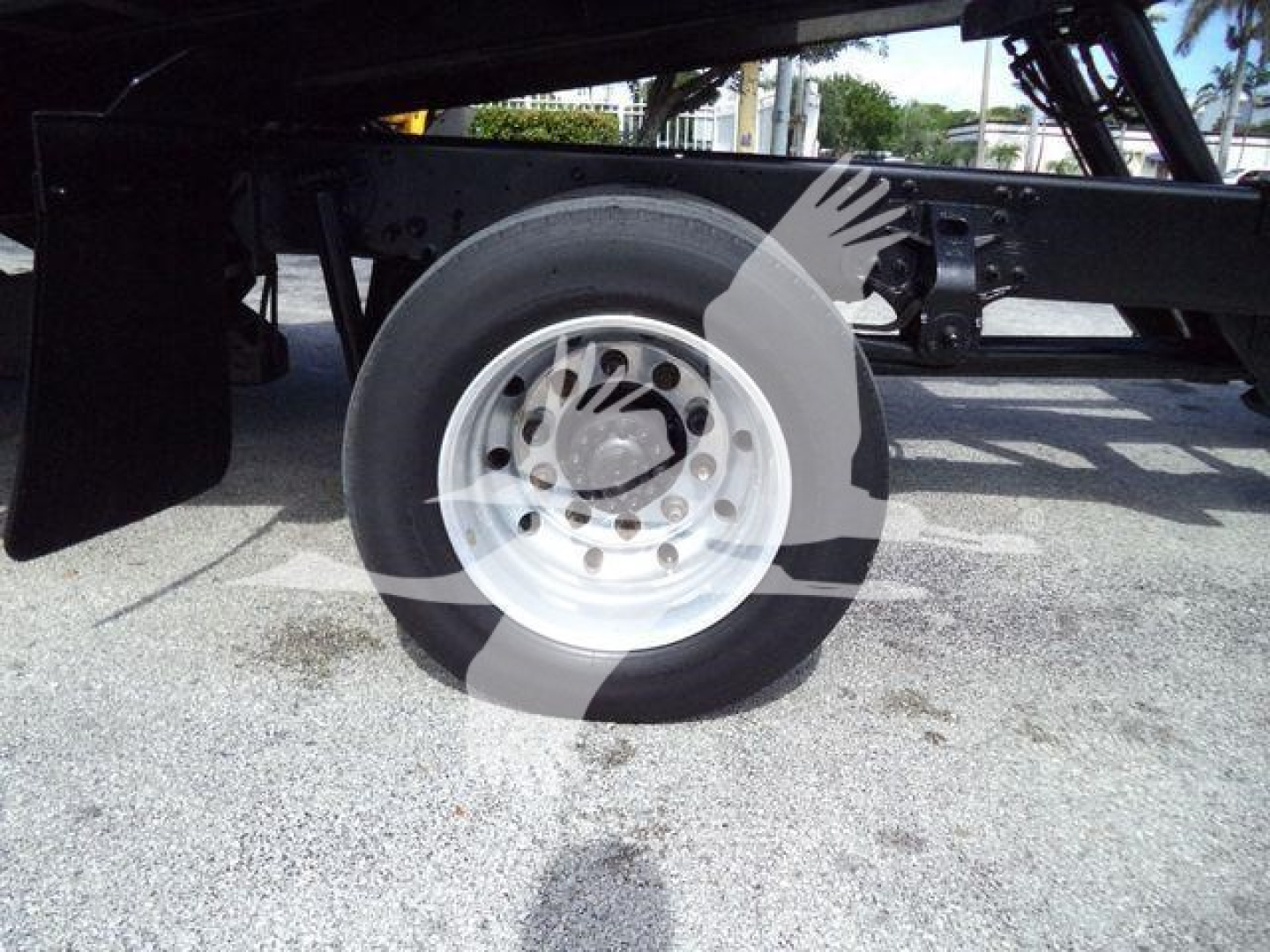 Wheel and undercarriage of a truck chassis with a white steel wheel and tire, visible frame components and gravel ground.