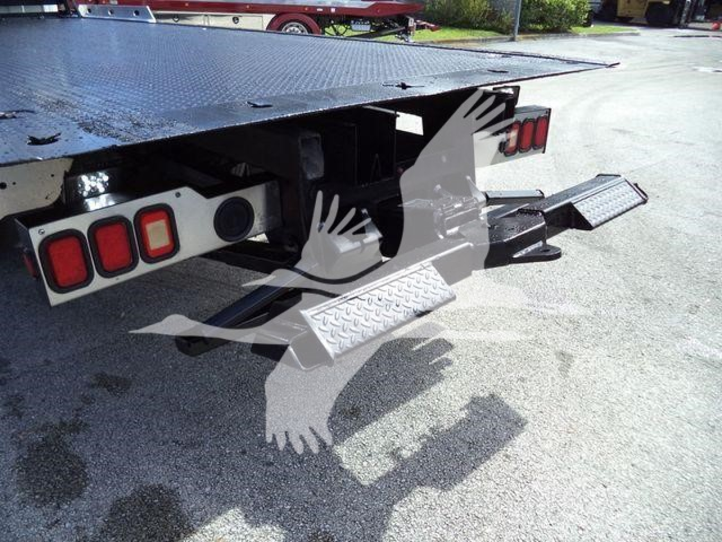Rear view of a rollback truck showing the undercarriage and tow steps with dual rear lights and metal diamond plate ramp. There are no legible stickers or text visible.