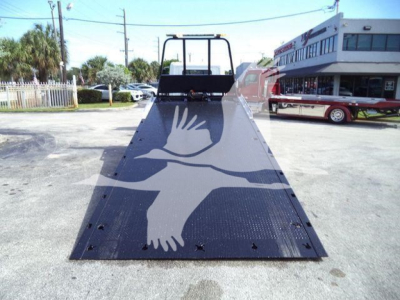 Truck bed with a large unfolded flatbed ramp in a parking lot showing a rear loading ramp with a white bird graphic on black metal surface.
