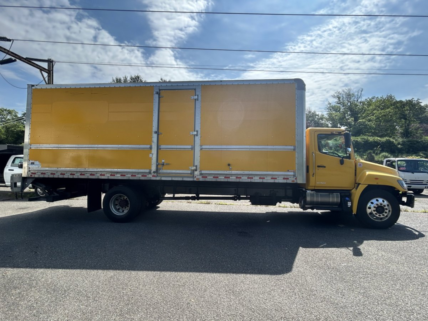Side view of a yellow 2020 Hino 338 box truck in a parking lot with long cargo box and cab, no visible branding text on doors.