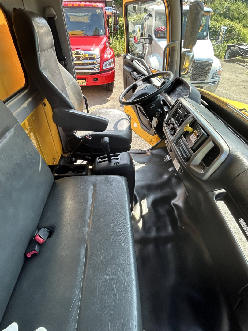 Vehicle cab interior of a 2020 Hino 338 box truck showing black vinyl seats, steering wheel, dashboard, and center console.
