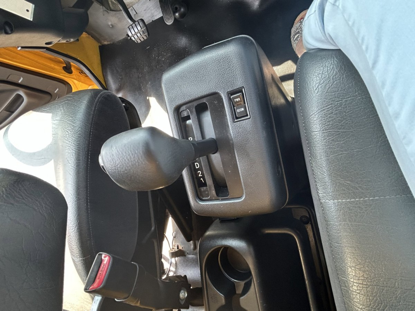 Vehicle interior showing gear shifter with PRND2L labels and cup holder area; seating visible.