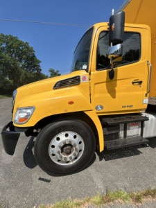 Side view of a yellow 2020 Hino 338 box van truck showing cab and front wheel, with VIN/stock info not visible on the image.