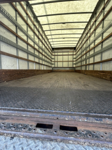 Truck cargo space of a 2020 Hino 338 with empty box, metal floor, side walls with horizontal support rails.