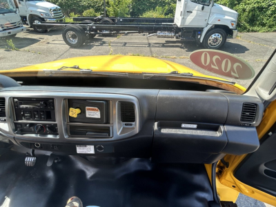 Dashboard and interior view of a yellow 2020 Hino 338 box van from the passenger side, with a stickered 2020 tag on the windshield, and a view of the exterior cab and chassis.