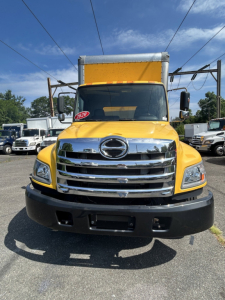 Front view of a yellow 2020 Hino 338 box truck showing chrome grille, Hino emblem, large black bumper, windshield, side mirrors, and cab with a raised box.