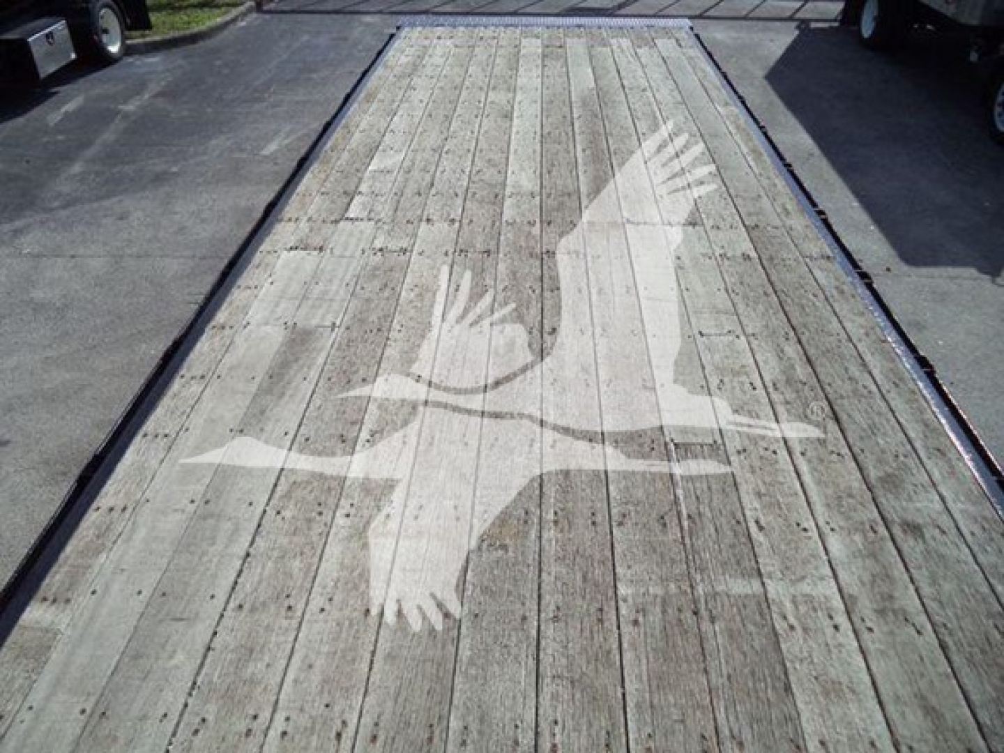 Flatbed truck deck with a faded white bird graphic (two wings) painted on wooden planks.