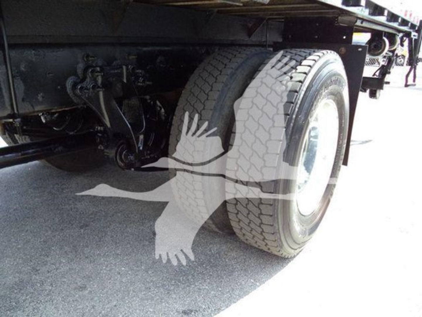 Flatbed truck rear view showing dual rear tires and undercarriage components.