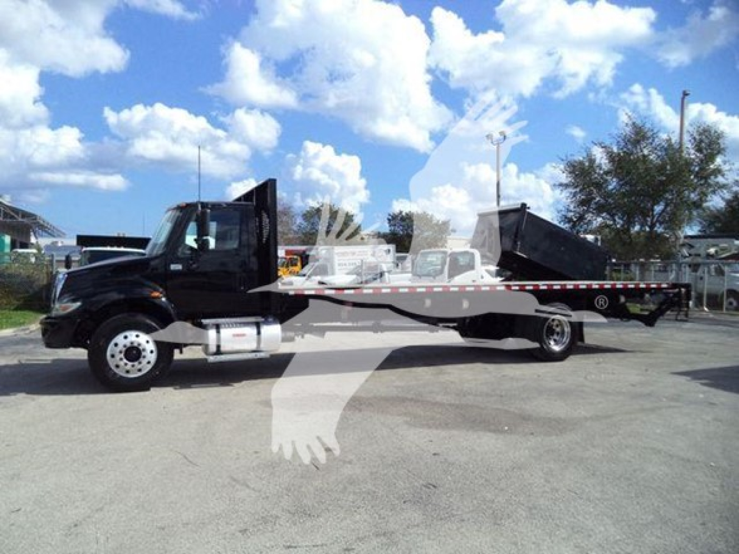 Flatbed tow truck side view showing 2019 International Durastar 4300 with black cab and long black flatbed, cargo bed rear, chrome wheels, clear sky.