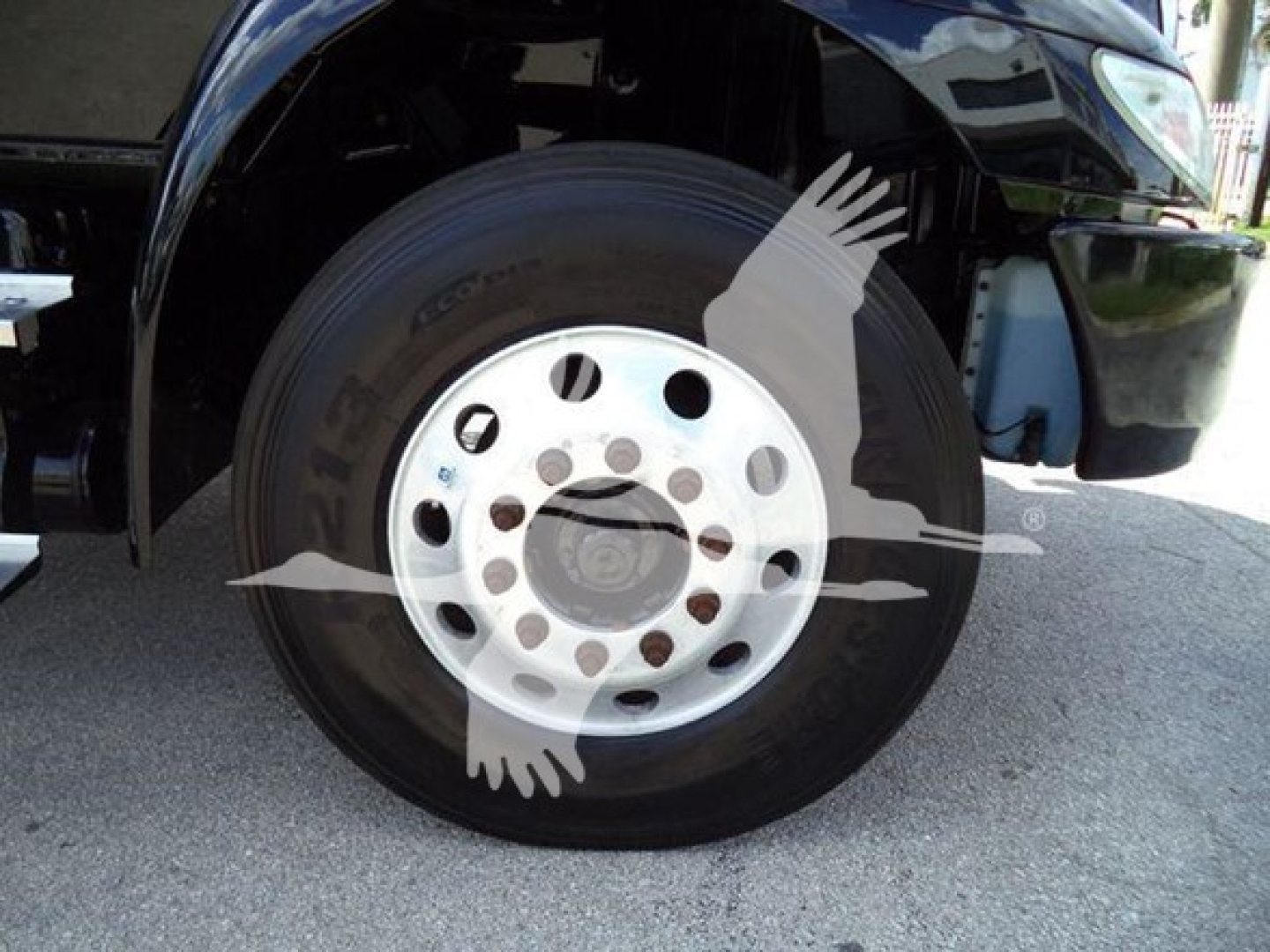 Truck wheel showing steel rim and black tire with partial fender and blue DEF reservoir in background