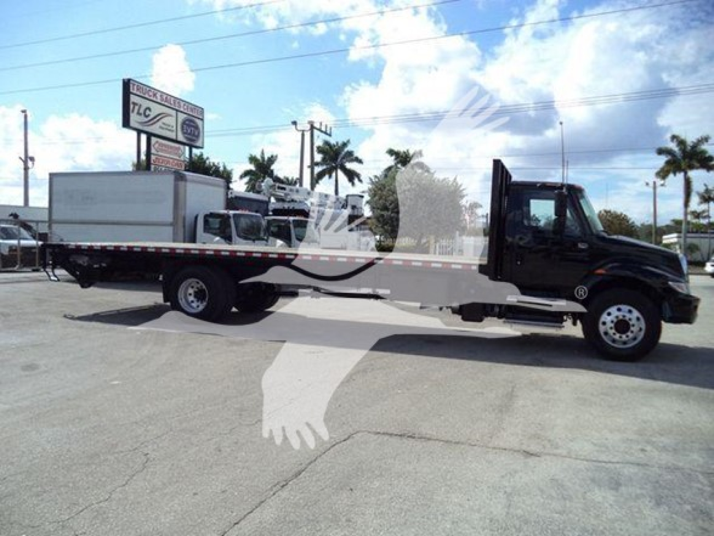 Flatbed tow truck with black cab and long white flatbed, International Durastar 4300, side view in a parking lot.