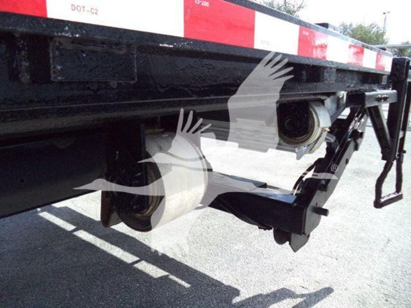 Flatbed truck undercarriage showing dual rear wheels and receiver/brace components under trailer; visible wheel hubs and suspension area.