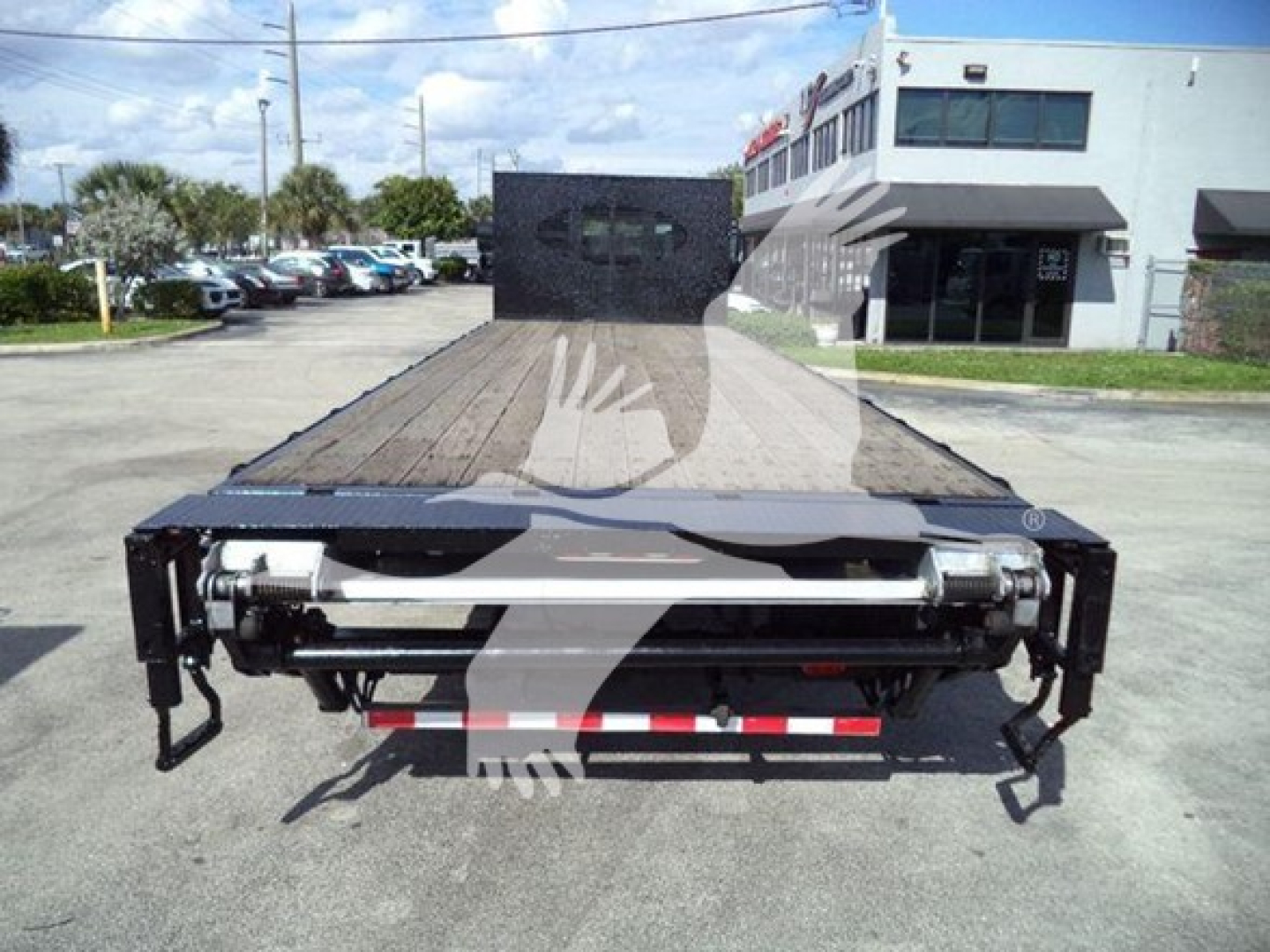 Flatbed tow truck rear view showing wooden deck and hydraulic winch system with dual rear bumper supports and light-duty frame.