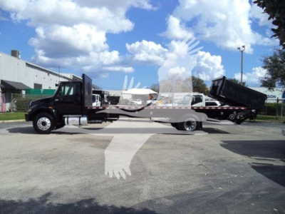 Truck: 2019 International Durastar 4300 flatbed. Side view showing black cab, long flatbed, and a dump trailer in the bed. VIN 1HTMMMML5KH584209 is visible in listing text, not on vehicle.