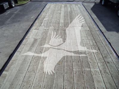 Flatbed truck deck with a faded white bird graphic (two wings) painted on wooden planks.