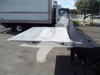 Flatbed truck loading ramp extended from a durastar 4300 chassis showing a metal ramp with screws and hinge by the flatbed edge.