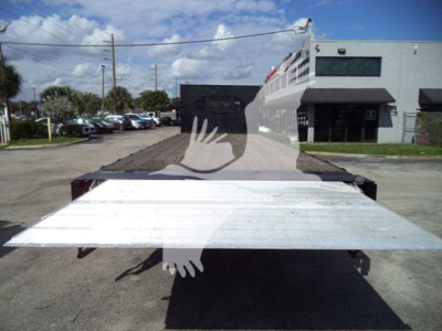Flatbed truck bed of a 2019 International Durastar 4300 with a metal ramp folded down in the foreground; dealership building and other trucks visible in background.