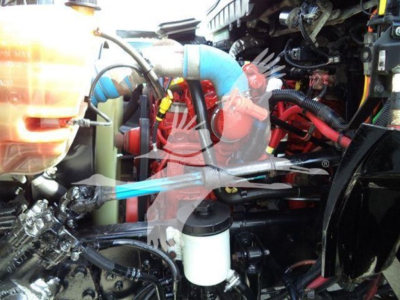 Engine bay of 2019 International Durastar 4300 flatbed showing coolant reservoir, blue coolant hose, white plastic filter canister, and various hoses.