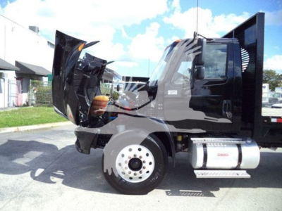 Trucking cab with hood open showing damaged front area and large fuel tank on the side. Flatbed truck, International Durastar 4300, black cab, chrome wheel, silver fuel tank, side steps visible.