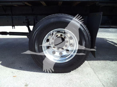 Flatbed truck wheel and tire under chassis; steel rim with lug nut holes visible, undercarriage and suspension components