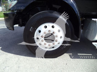 Wheel and front suspension area of a 2019 International Durastar 4300 flatbed truck showing front wheel with white steel rim and tire, partial bumper and frame.