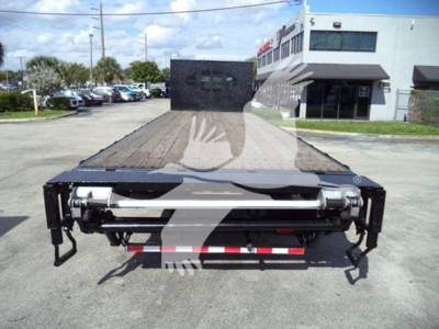 Flatbed tow truck rear view showing wooden deck and hydraulic winch system with dual rear bumper supports and light-duty frame.