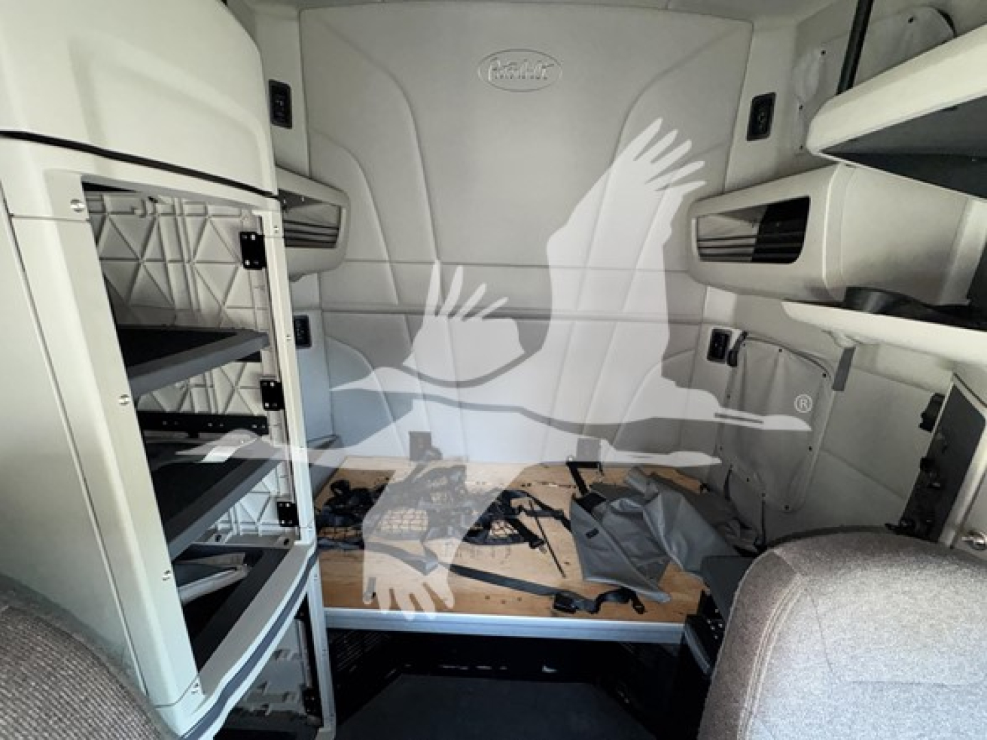 Peterbilt 579 truck cab interior showing sleeper area with storage compartments and shelves on left, fabric seats partially visible, VIN and stock info not visible in panel.