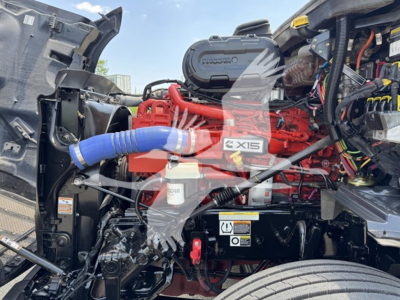 Peterbilt 579 engine bay with red engine, blue intake hose, and various wiring; visible labels and components including air intake, coolant reservoir, and warning sticker.