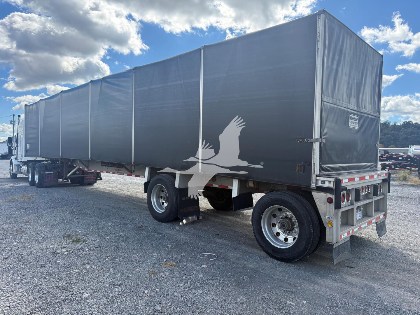 Semi trailer with curtainside black cover and white crane graphic on side; rear shows reflective safety trim, tail lights, and bumper.