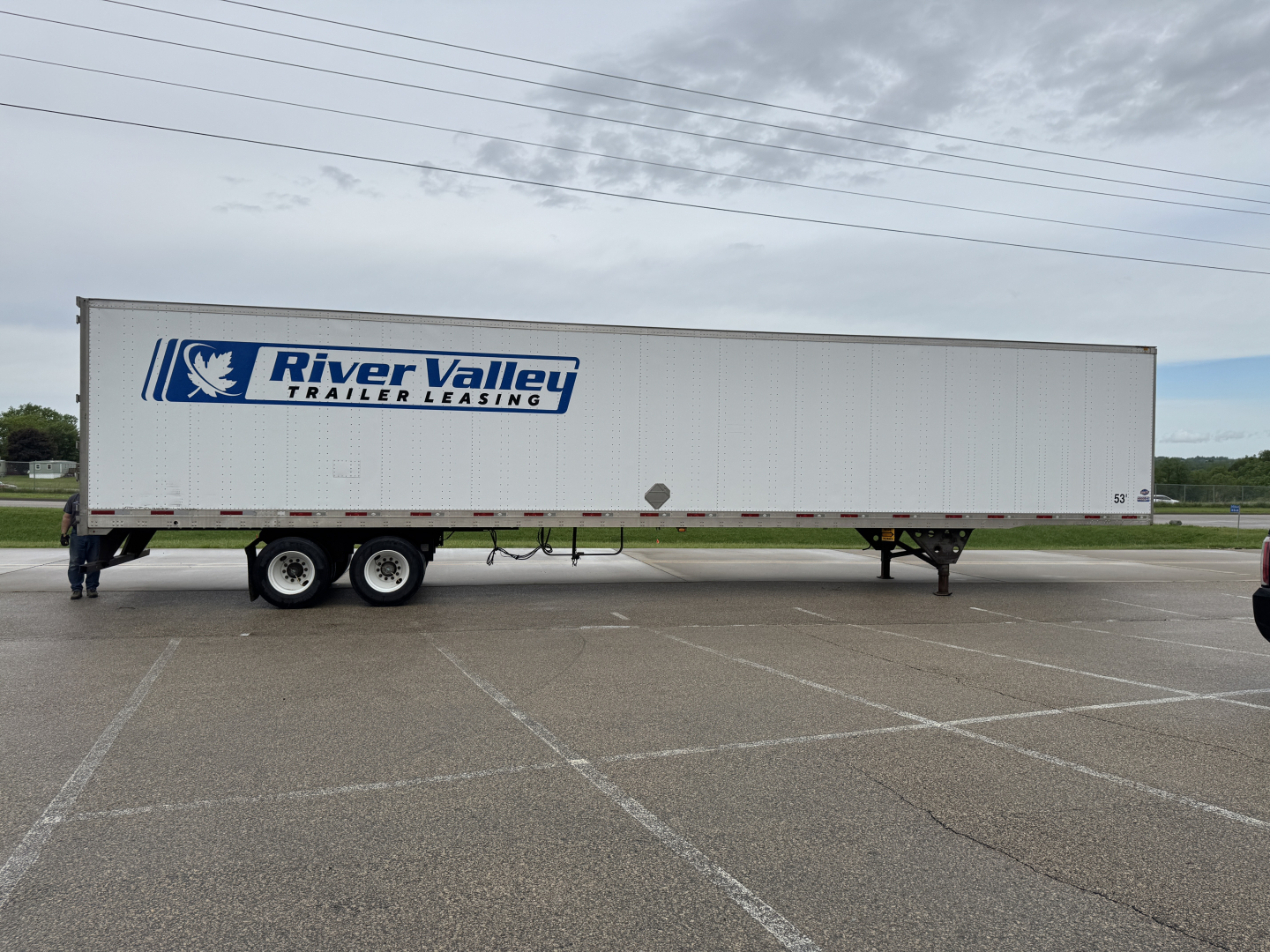 Trailer side view showing River Valley Trailer Leasing logo on a white utility trailer with dual rear axles in a parking lot.