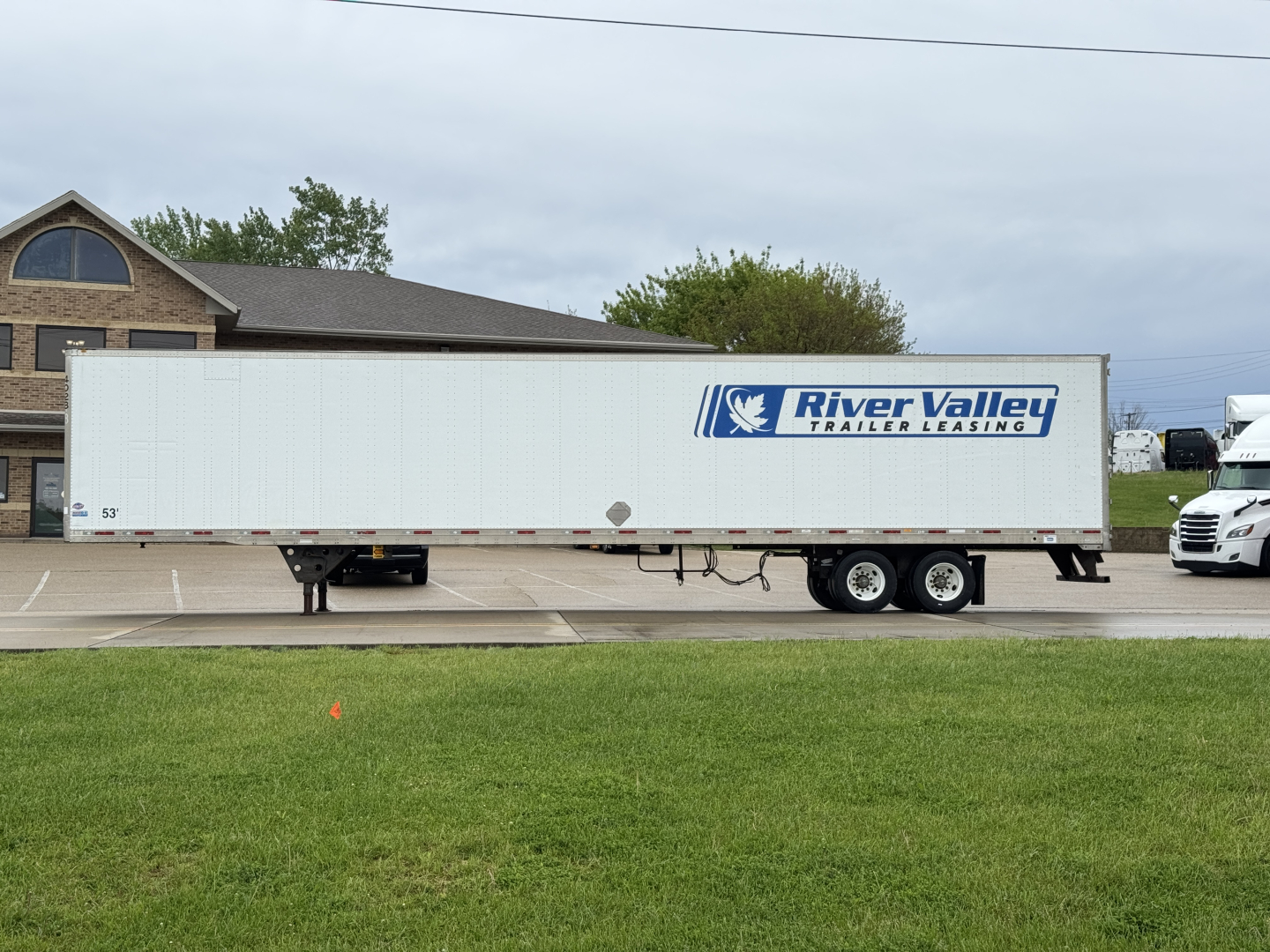 Trailer side view showing River Valley logo on white utility trailer with dual rear axles in a parking lot.