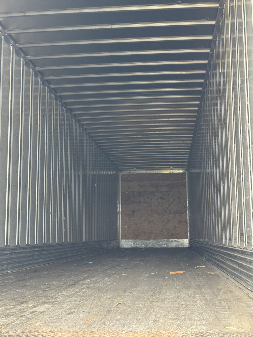 Flatbed trailer interior showing corrugated metal walls and wooden rear door; empty cargo space inside.
