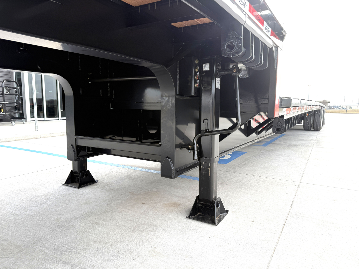 Trailer landing gear and underside of a 2027 Dura Haul drop deck trailer showing legs and steel frame with hydraulic components.