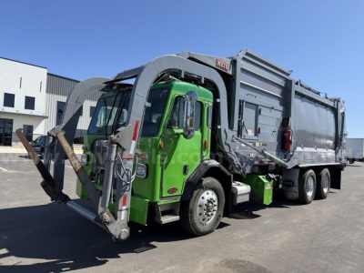 Green Peterbilt 520 garbage truck with front loader, side view showing hopper and chassis in-service