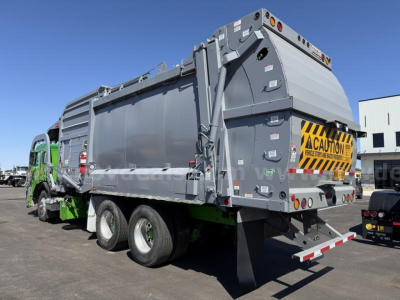 Peterbilt 520 garbage truck rear and side view showing large gray hopper with caution signage and dual rear wheels.