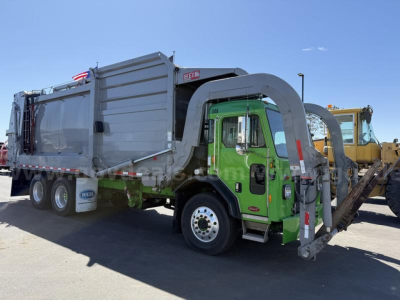 Peterbilt 520 hooklift garbage truck in service showing rear grapple and green cab with gray body and dual rear wheels.
